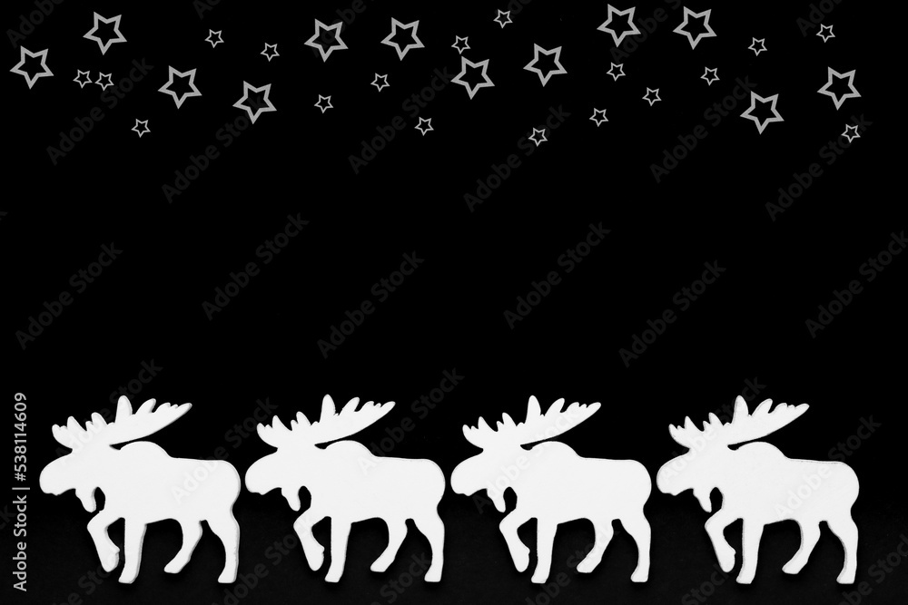 White wooden reindeer on a black background, top border with white stars, christmas silhouette. Top view, copy space. White wooden reindeer on a black background, top border with white stars, christmas silhouette. Top view, copy space.