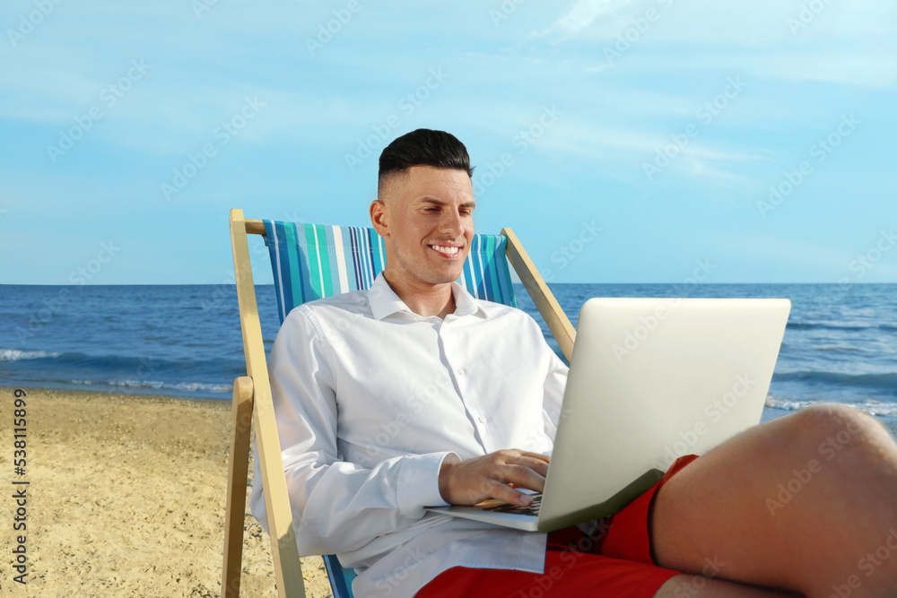 Happy man working with laptop on beach. Business trip