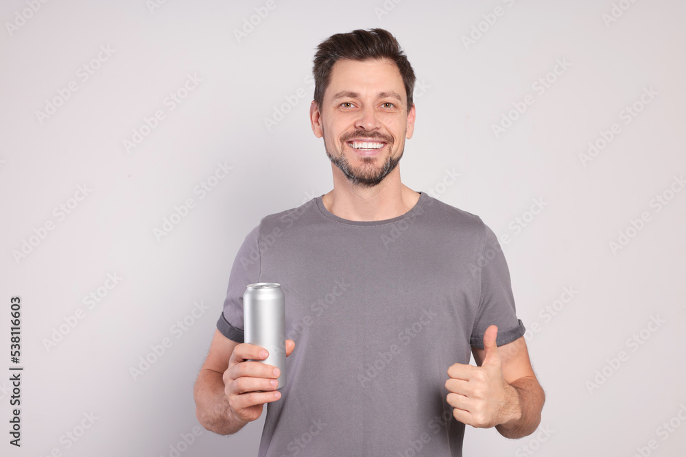 Happy man holding tin can with beverage on light grey background Happy man holding tin can with beverage on light grey background