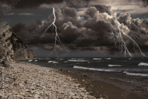 Dark cloudy sky with lightnings over sandy beach with rocks and sea. Thunderstorm