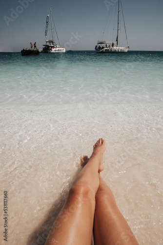 Fototapeta Naklejka Na Ścianę i Meble -  Kobiece nogi na plaży z widokiem na łodzie