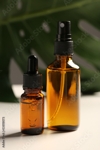 Bottles with oil and green leaf on white table. Natural cosmetics
