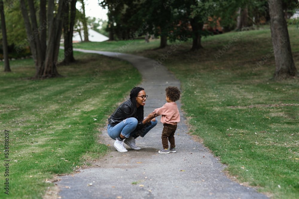 Black mother walking on sidewalk with biracial toddler
