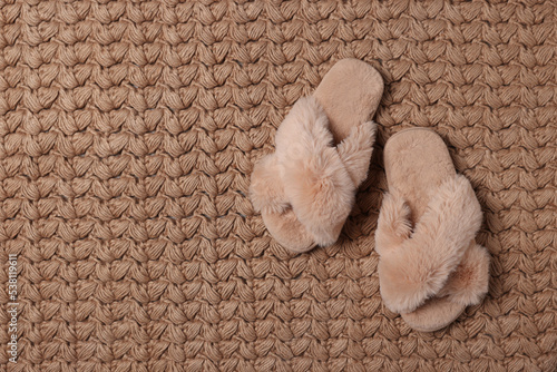 Fluffy beige slippers on soft carpet, top view. Space for text