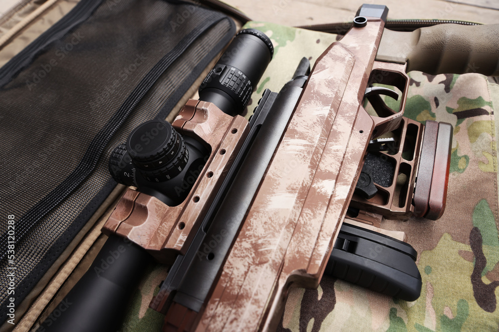 Modern powerful sniper rifle with telescopic sight on camouflage fabric, closeup Stock Photo