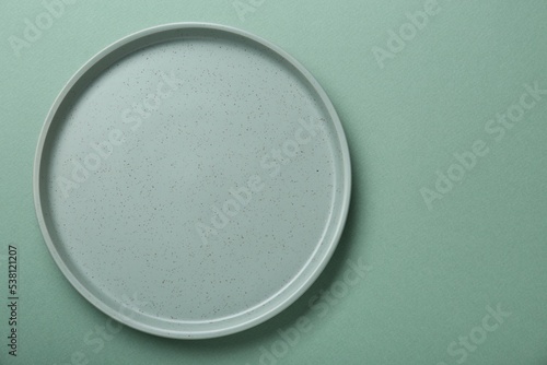 Empty ceramic plate on green background, top view. Space for text