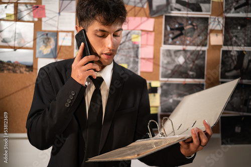 Fotografia Young detective reading dossier in dark office, calling on phone