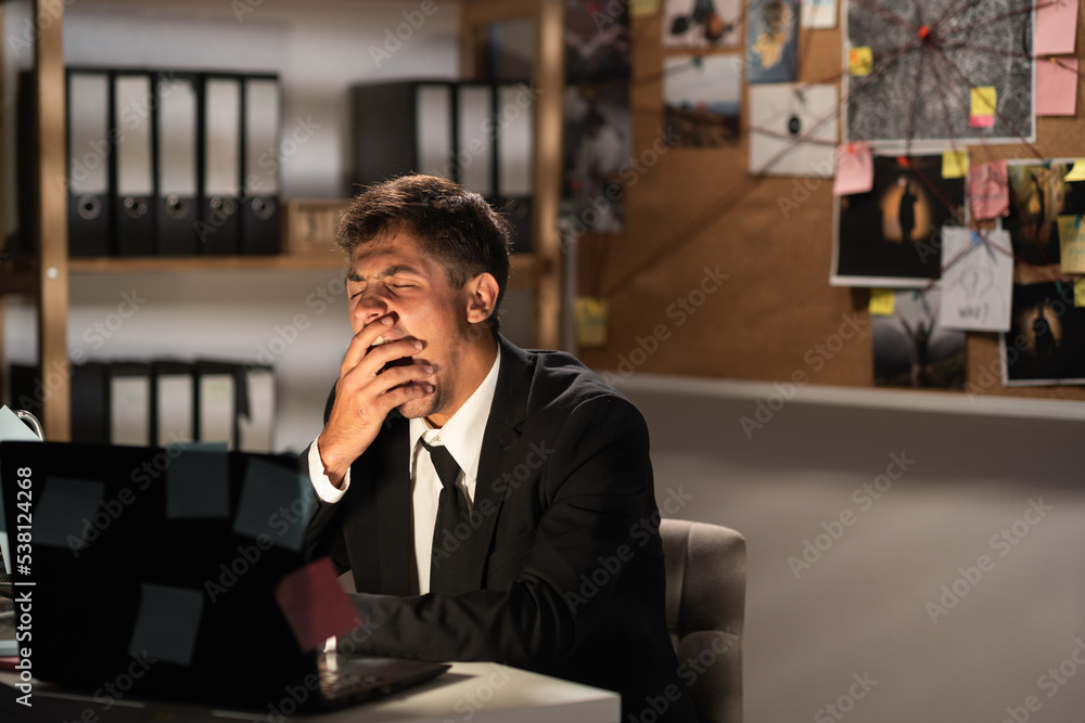 Young arabic detective working at his desk in an office late at night stressful in front using computer laptop yawning, businessman overtime work and yawn Young arabic detective working at his desk in an office late at night stressful in front using computer laptop yawning, businessman overtime work and yawn