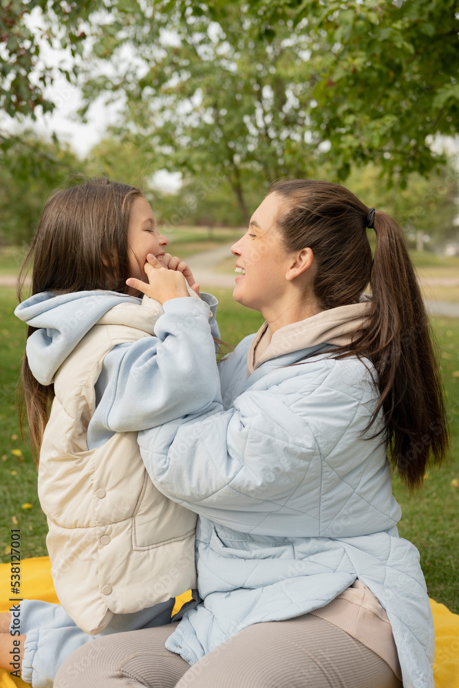 Mother and daughter hugging on blanket in park Mother and daughter hugging on blanket in park
