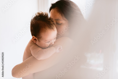 intimate portrait of hispanic mother holding newborn baby daughter in her arms showing love and care, with soft natural light. concept of bonding and motherhood