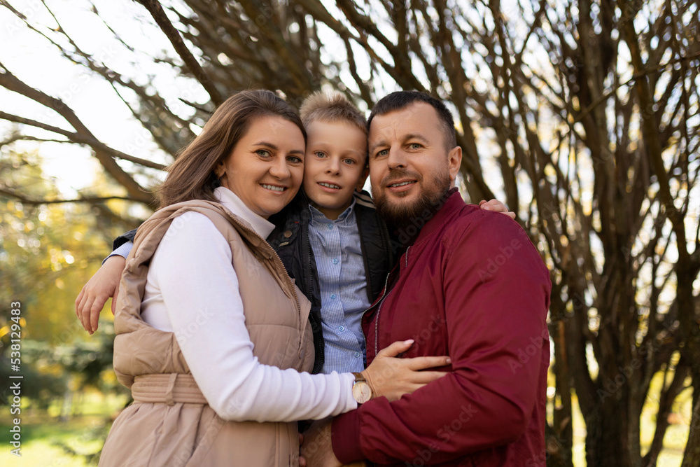 portrait of happy mom dad and son between them against the backdrop of an autumn park