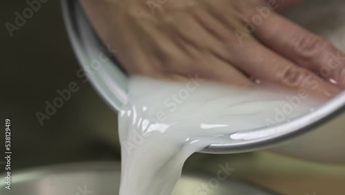 Washing raw white Thai jasmine long grain rice pouring out white cloudy starchy water liquid from the bowl in slow motion.