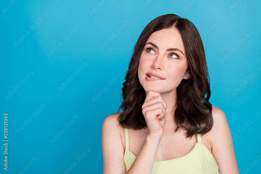 Photo of shiny unsure girl dressed green dress arm chin biting finger looking empty space isolated blue color background Photo of shiny unsure girl dressed green dress arm chin biting finger looking empty space isolated blue color background