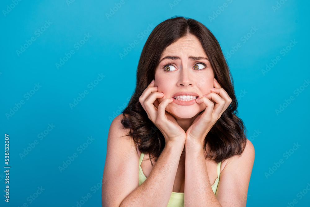 Photo of scared shocked lady wear green outfit looking empty space biting fingers isolated blue color background Photo of scared shocked lady wear green outfit looking empty space biting fingers isolated blue color background