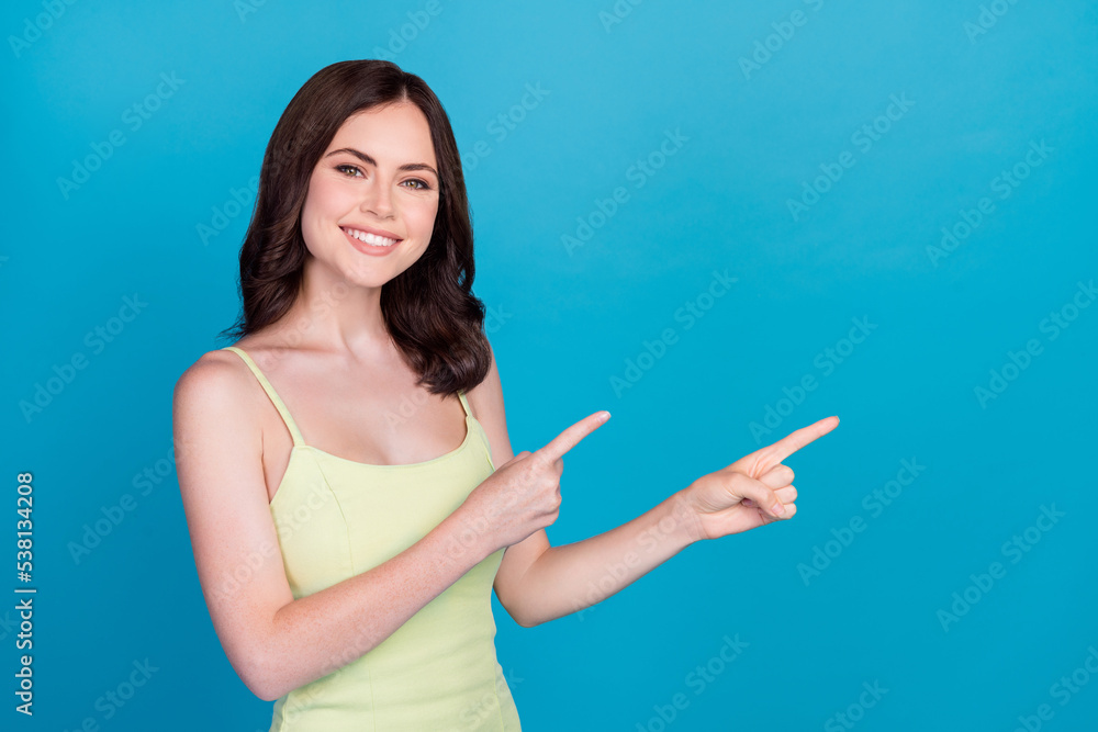 Photo of positive lovely cute person toothy smile indicate fingers empty space isolated on blue color background Photo of positive lovely cute person toothy smile indicate fingers empty space isolated on blue color background