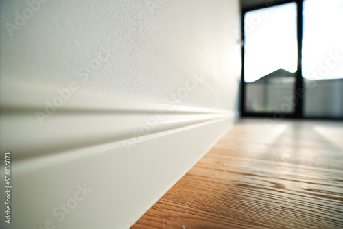 Obraz na plátně Detail view with a white wooden plinth at the corner of the parquet wall inside a new house with no furniture inside it