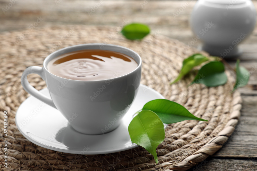 Green tea in white cup with leaves and wicker mat on table, closeup Green tea in white cup with leaves and wicker mat on table, closeup