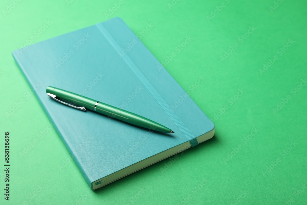 New stylish planner with hard cover and pen on green background New stylish planner with hard cover and pen on green background