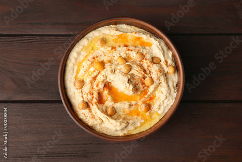 Bowl of tasty hummus with chickpeas and paprika on wooden table, top view