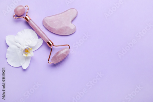 Gua sha stone, face roller and orchid flower on violet background, flat lay. Space for text