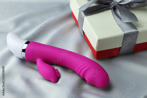 Gift box and pink vaginal vibrator on grey silk fabric. Sex toy photo