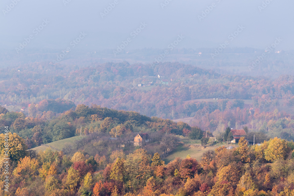 Village houses on hill surrounded with lush forest in autumn colours