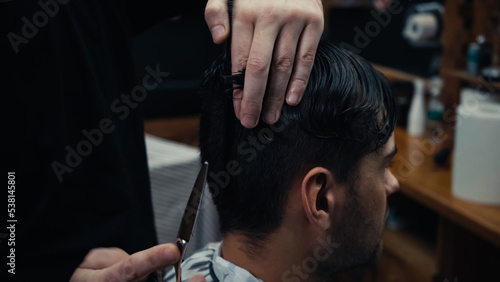 Hairdresser holding scissors and hair of client in hairdressing cape in salon.