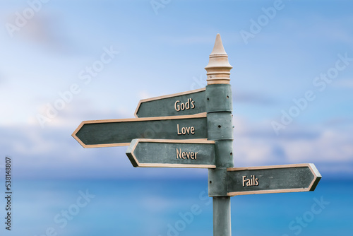 gods love never fails quote written on fancy steel signpost outdoors by the sea. Soft Blue ocean bokeh background.