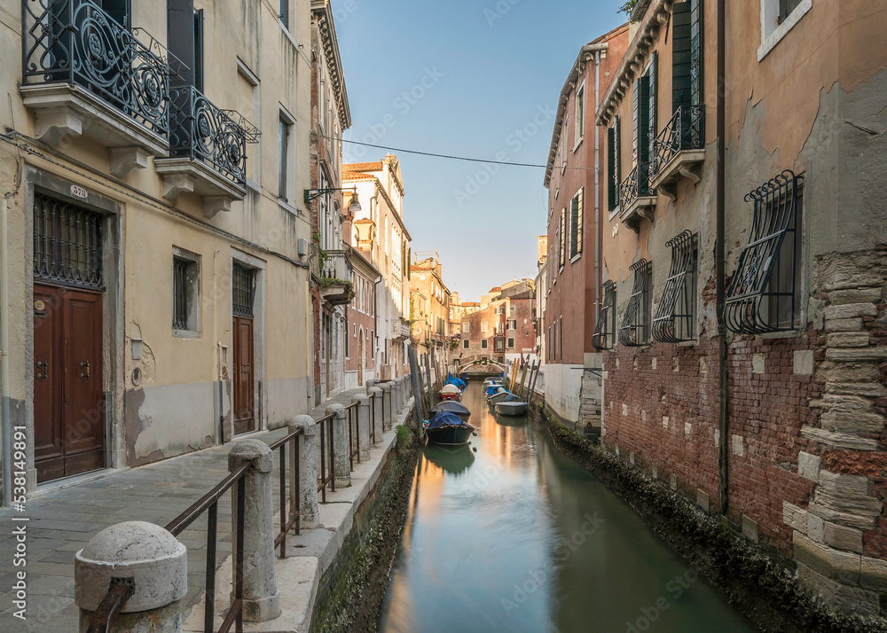 Typical Venetian canal, early in the morning. Venice, Italy. The buildings are reflecting on the calm water