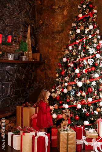 Christmas little happy girl and Santa's dog near a huge Christmas tree with gifts.