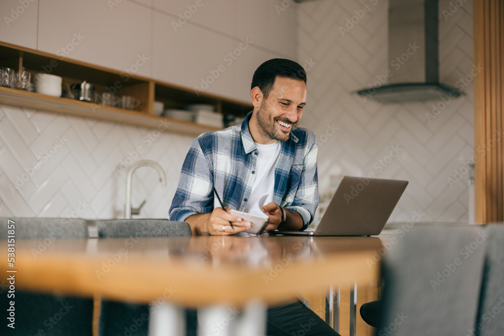 Smiling businessman working from home, looking at the laptop, writing some notes. Smiling businessman working from home, looking at the laptop, writing some notes.