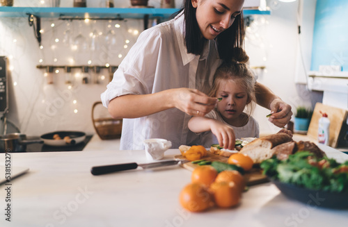Cheerful mother and daughter preparing breakfast at kitchen