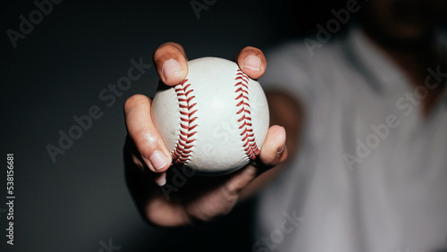 Selective focus of man holding baseball ball isolated on black background.