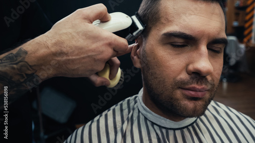 Tattooed barber trimming hair of man in barbershop.