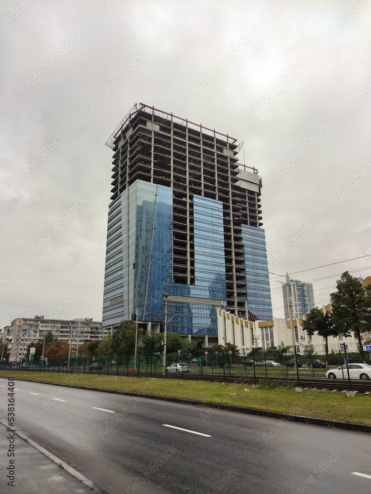 A huge unfinished skyscraper with glass walls on the background of an asphalt road
