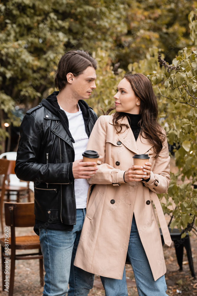 Fototapeta premium young woman and man in stylish outfits holding coffee to go and looking at each other.