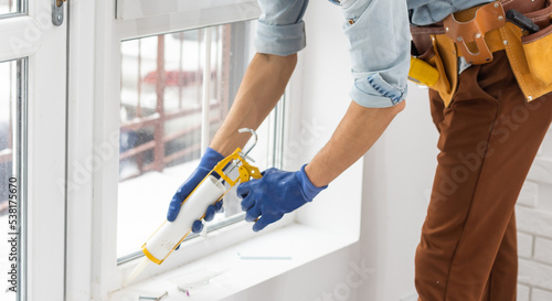Construction worker sealing window with caulk indoors