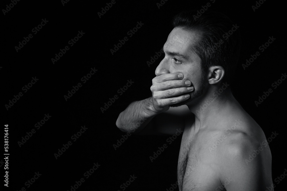 The man covers his mouth with his hands. Black-white portrait of a man on a black background. The man covers his mouth with his hands. Black-white portrait of a man on a black background.