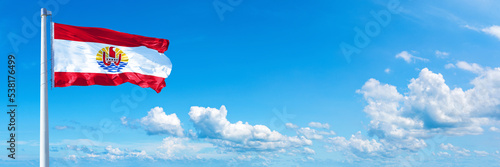 French Polynesia flag waving on a blue sky in beautiful clouds - Horizontal banner photo