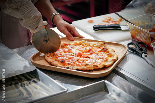Chef cuts freshly prepared pizza slices at kitchen