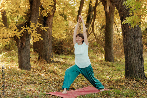 An elderly woman practices yoga in the autumn forest © Iuliia