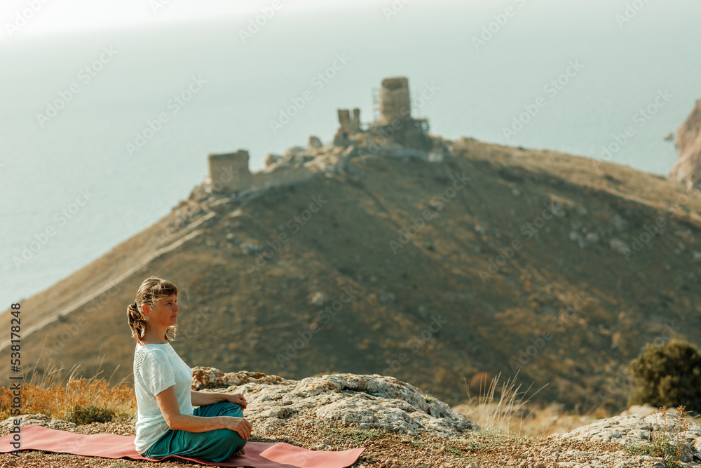 An elderly woman practices yoga on a mountain overlooking the sea