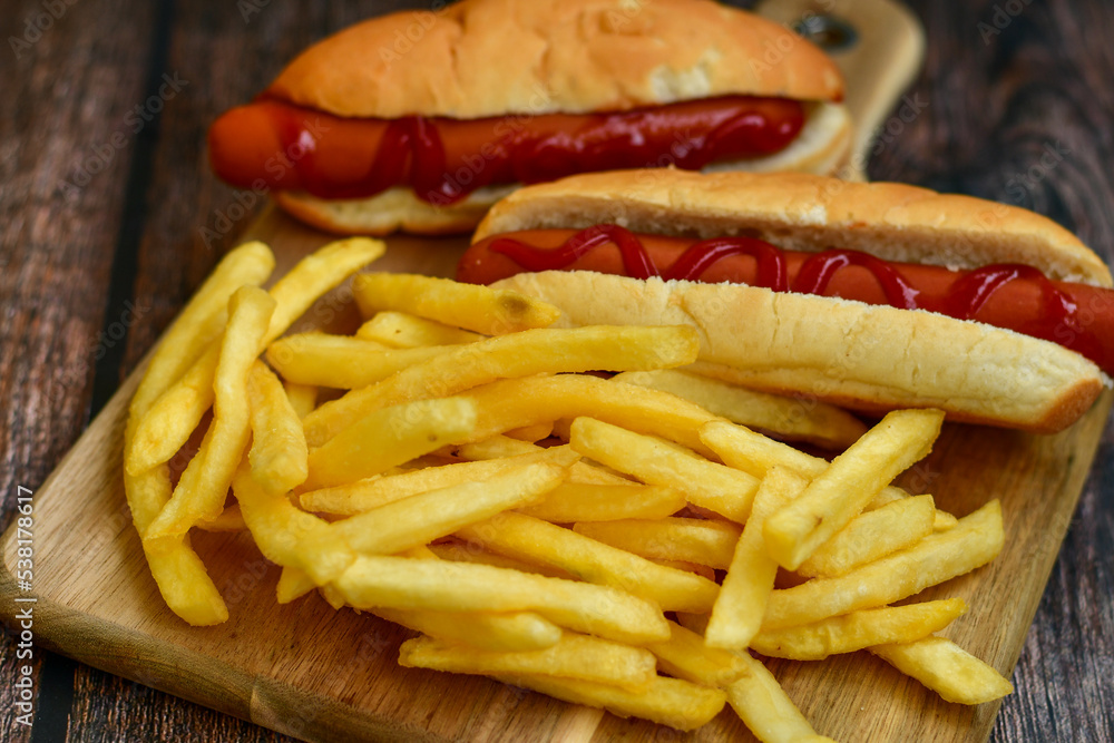 Tasty Hot dogs and deep fried french fries on paper on wooden background Tasty Hot dogs and deep fried french fries on paper on wooden background