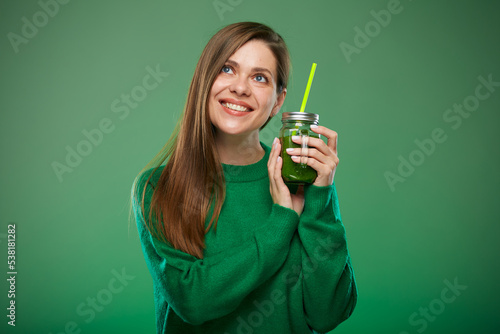 Young woman wering green sweater holding smoothie jar with drink looking up. Isolated female advertising portrait on green.
