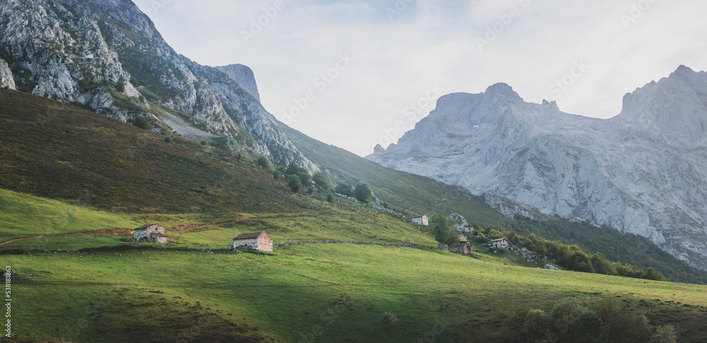 Beautiful mountain landscape with a few cabins in the green hill and the mountains at the bottom