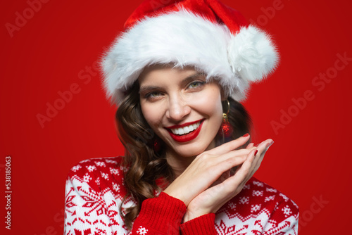 Portrait of woman in santa hat and christmas sweater posing on red background