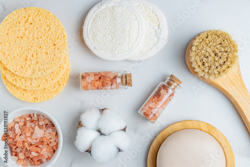 personal hygiene tools and cosmetics on white background. Face soap, brush with natural bristle. pink himalayan salt in a bowla, cotton and lufa reusable sponges for skin cleanser.