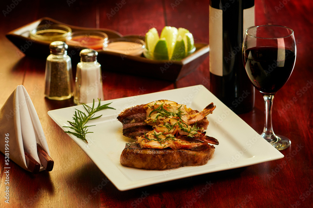 Elegant Grill baked Sirloin, tenderloin, steak served with shrimp and bottle of wine on a wooden table in a square white plate.
