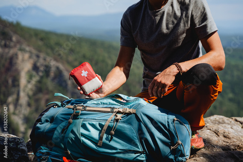 A person holds in his hand a first-aid kit, tourist equipment, a hiking backpack, a red first-aid kit in the mountains, a collection of equipment
