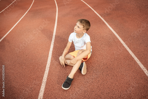 boy in white T-shirt is sitting on the stadium's treadmill. Selective focus, copy space © Liubov Sokolova